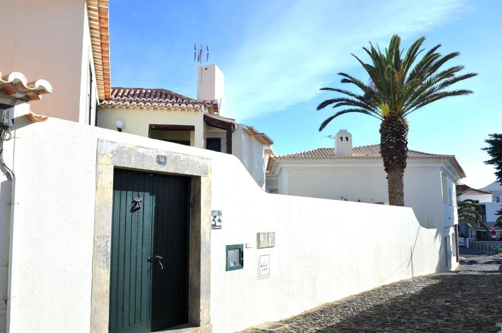 The whitewashed house with its green gate, number 16, and a palm tree on a cobbled street